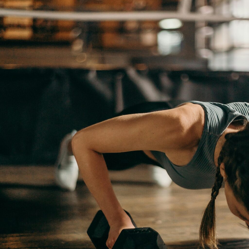 Fit woman doing a dumbbell push-up in a gym, highlighting strength and fitness training.