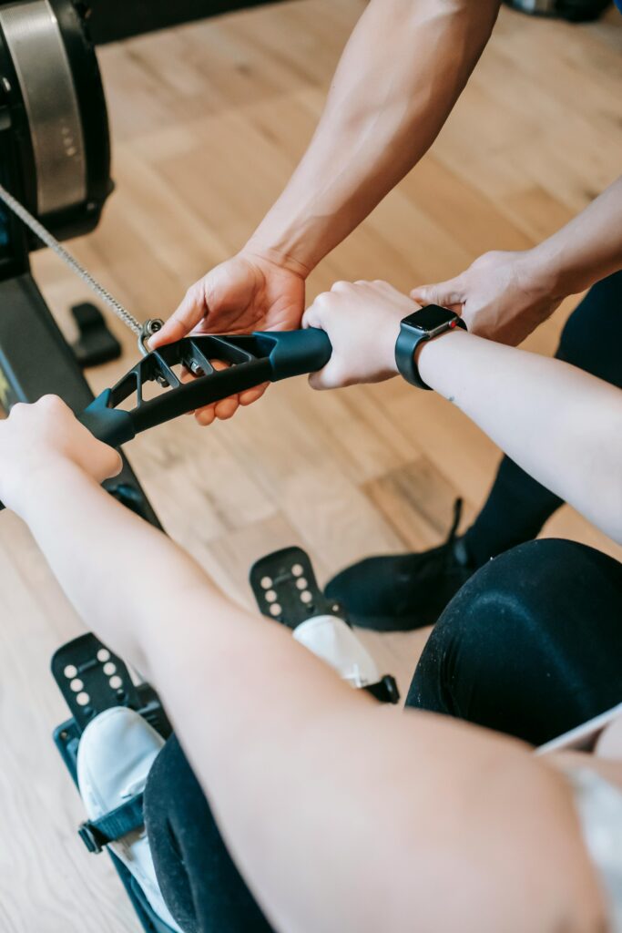pexels-photo-6551429-6551429 High angle of crop anonymous trainer assisting woman exercising on rowing machine in sports club